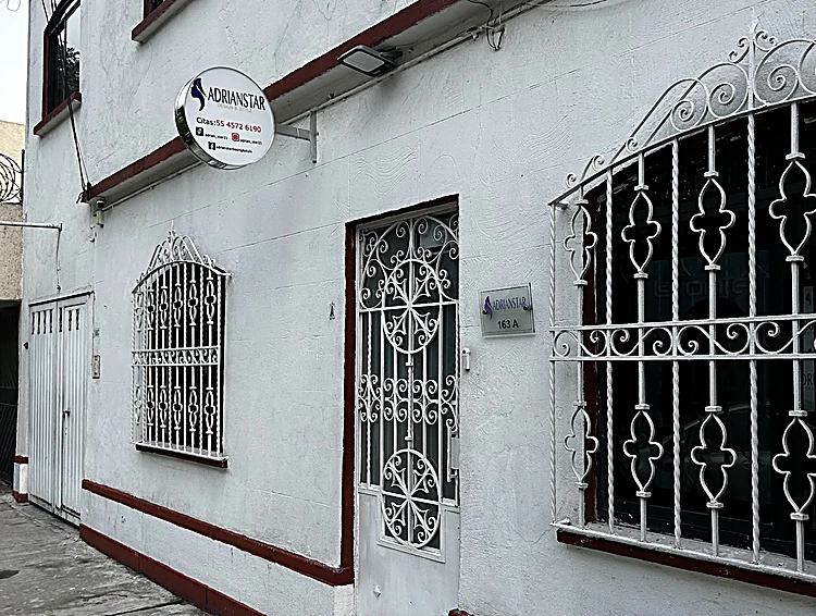 Fachada blanca con rejas de herrería, franja roja abajo y el letrero redondo de ADRIANSTAR sobre la puerta