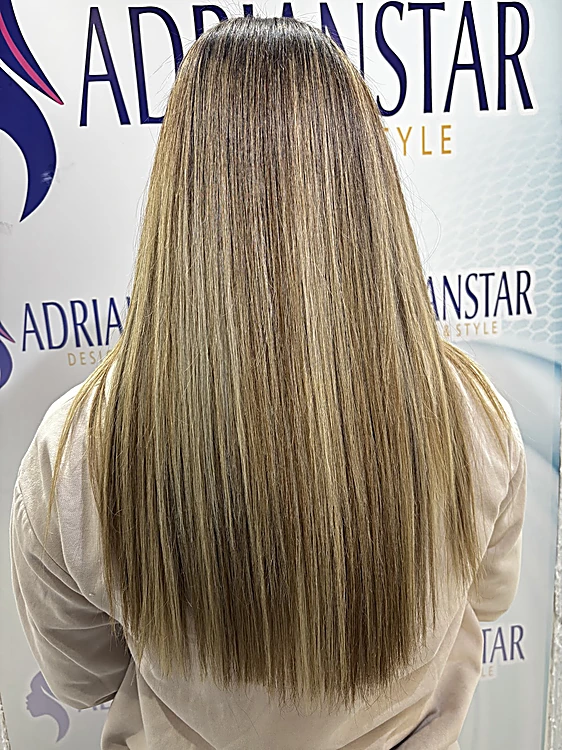 Mechas rubias sobre castaño en cabello largo y lacio, frente al telón de ADRIANSTAR