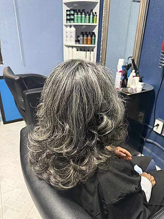 Cabello plata y gris en capas con volumen, de espaldas en un sillón del salón junto a la pared azul