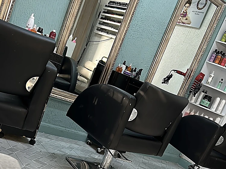 Interior del salón: sillones negros frente a espejos con marco plateado, pared azul acero y piso de mosaico en espiga con luz de ventana