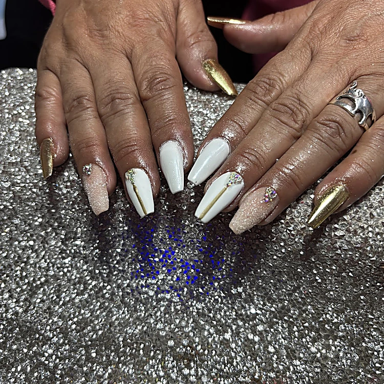 Uñas largas de acrílico blancas, nude y doradas con cristales, sobre la mesa de brillantina