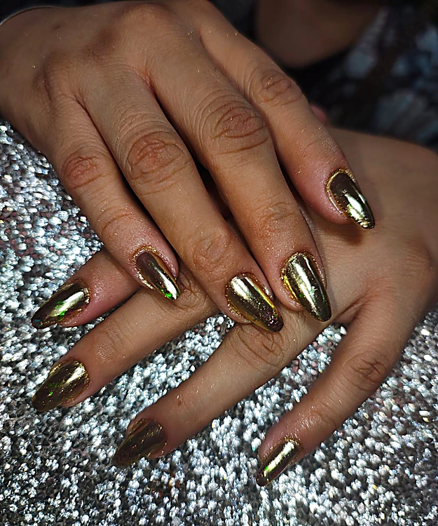 Uñas almendra con efecto espejo dorado sobre la mesa de brillantina plateada
