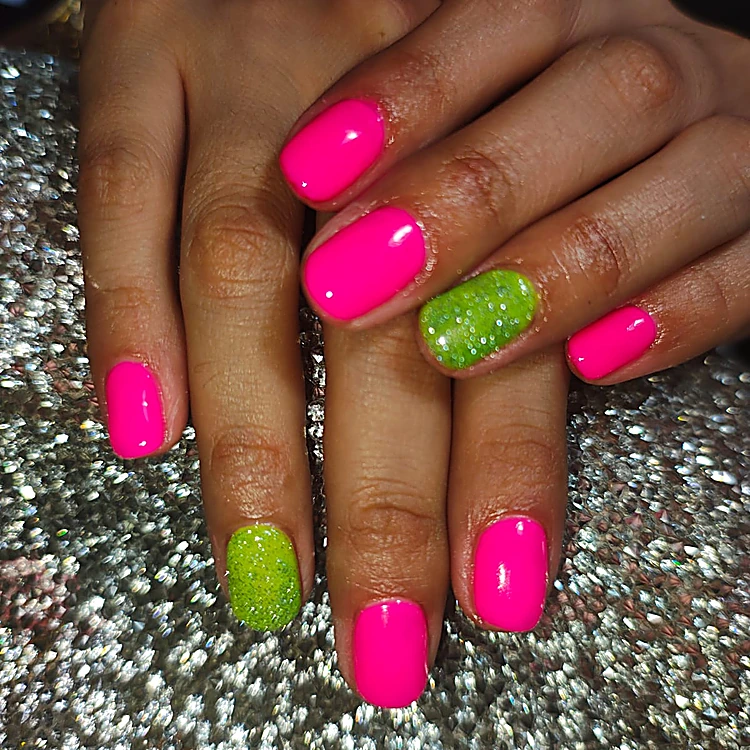 Uñas cortas rosa neón con dos uñas de brillantina verde, sobre la mesa plateada