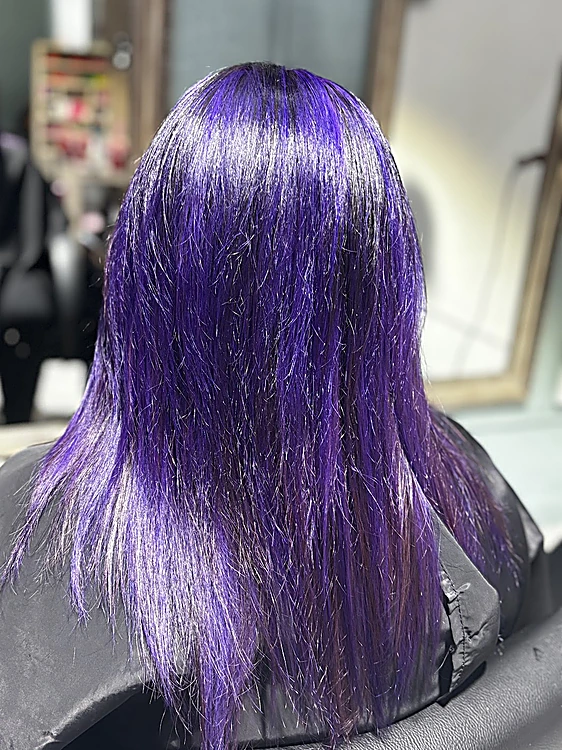 Cabello lacio violeta intenso, de espaldas frente al espejo del salón