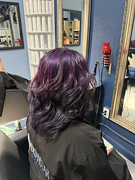 Violeta oscuro en ondas a la altura del hombro, con la capa negra de ADRIANSTAR, frente al espejo